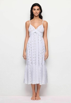 Witte katoenen jurk met verstelbare spaghettibandjes, een gedraaid voorkruis en een bloemen geperforeerd patroon. Uitlopende zoom eindigt onder de knie.