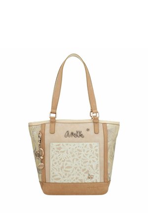 Sac fourre-tout beige avec motif floral brodé, accents en cuir, doubles poignées et charms décoratifs. Texture lisse avec une forme structurée.