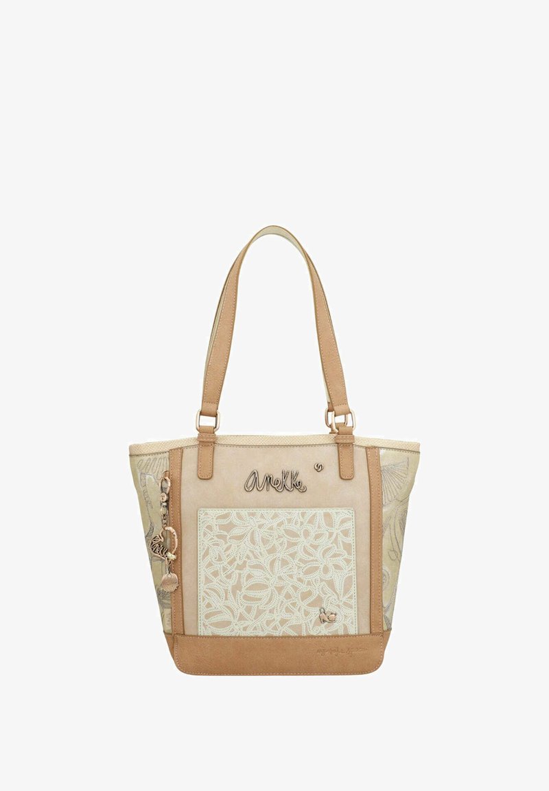 Sac fourre-tout beige avec motif floral brodé, accents en cuir, doubles poignées et charms décoratifs. Texture lisse avec une forme structurée.