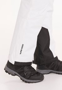 Witte waterdichte broek met zwarte accenten, voorzien van een logo met de tekst "WPRO 10000" aan de zijkant, gecombineerd met zwarte wandelschoenen.