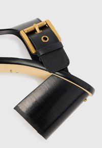 Sandal in pelle nera con tacco, punta quadrata, dettaglio della fibbia dorata e tacco a blocco texturizzato. Finitura liscia con accento del logo dorato.