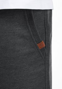 Pantalon de survêtement gris foncé en tissu doux, avec des poches latérales et une petite étiquette en cuir marron. Design simple et ajusté.