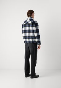 Plaid jacket in white, blue, and black fleece, featuring a collar and elastic cuffs; paired with dark denim pants and black shoes.