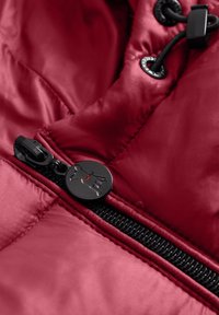 Zwarte rits met een ronde charm met een hondensilhouet op een rood gewatteerd jack stof close-up.