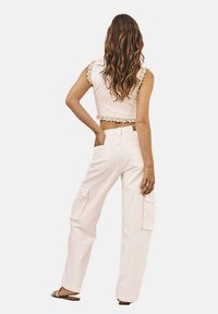 Top corto blanco con encaje en los bordes, combinado con pantalones cargo blancos que cuentan con bolsillos espaciosos y un corte relajado. Se lleva con sandalias planas.