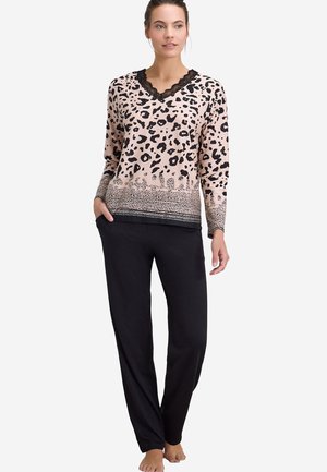 Femme portant un haut à manches longues rose imprimé léopard avec bordure en dentelle noire et un pantalon noir décontracté, debout pieds nus sur fond blanc.