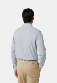 Camicia button-up a righe blu chiaro con colletto, maniche lunghe e vestibilità rilassata, abbinata a pantaloni beige. Tessuto con una consistenza liscia.