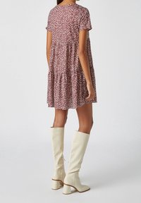 Vestido de estampado floral en burdeos con mangas cortas y diseño en capas, combinado con botas blancas de altura hasta la rodilla con tacón bloque y cremallera trasera.