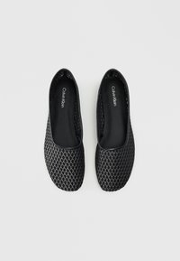 Scarpe nere basse con un motivo tessuto testurizzato, leggero splendore e design a punta arrotondata. La soletta presenta il nome del marchio, Calvin Klein.