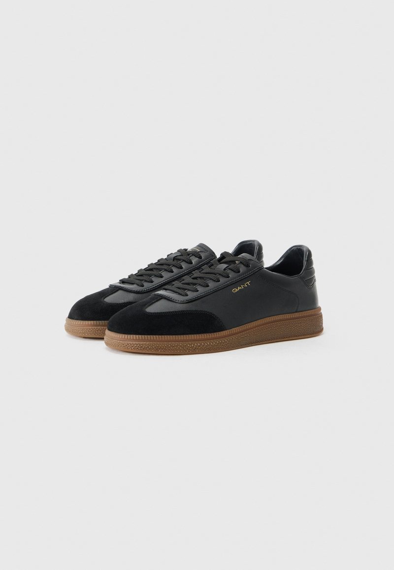 Baskets noires avec un dessus en daim et en cuir, dotées d'une semelle en gomme texturée, de lacets plats et d'un branding subtil sur le côté.