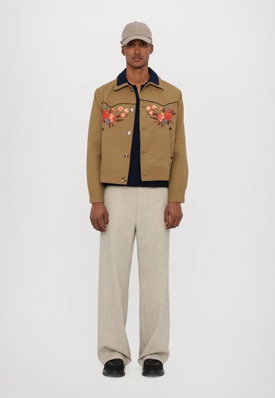 Khaki jacket with floral embroidery, dark blue collar, buttons, paired with light beige wide-leg trousers and black shoes.