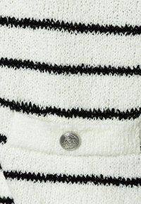 Tissu blanc texturé avec des rayures noires, présentant un détail de bouton argenté sur une poche. Le matériau semble doux et tricoté.
