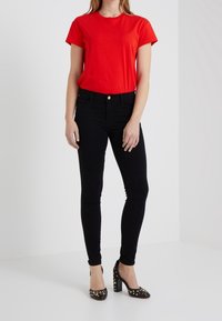 Red cotton t-shirt with short sleeves, paired with black skinny jeans. Black high heels with studded accents complete the outfit.