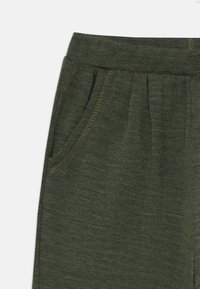 Närbild av mörkgröna stickade byxor som visar elastisk midjeresår och framficka med synlig sömnad.