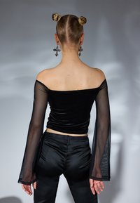 Top nero senza spalline con maniche lunghe trasparenti e corpo in velluto attillato, abbinato a pantaloni neri slim. Orecchini grandi a forma di croce inclusi.