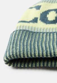 Gorro de malha com um esquema de cores em amarelo pastel e verde, com um punho canelado em azul escuro e um padrão geométrico no corpo.