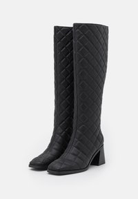 Bottes noires jusqu'aux genoux avec un motif matelassé, bout rond et talon épais. Fabriquées en matériau synthétique lisse avec une finition texturée.