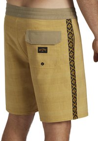 Shorts de bain à carreaux jaunes pour homme avec des bordures noires contrastantes sur les côtés, dotés d'une poche arrière et d'une étiquette tissée. Fabriqués en tissu léger.