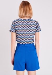 Chemise à manches courtes avec un motif zigzag en bleu, marron et beige, associée à un short bleu taille haute avec des poches avant.