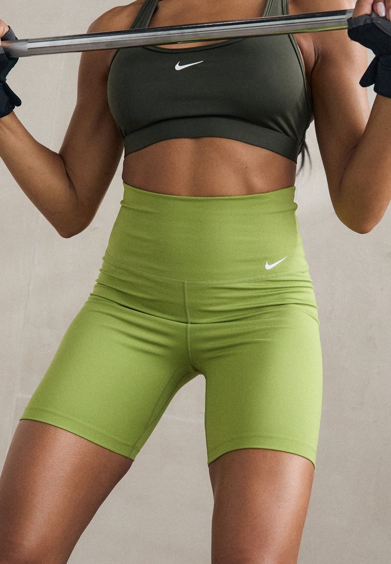 Pantalones cortos deportivos verdes de cintura alta, hechos de material elástico, con un logo blanco de Nike en la cintura y un diseño liso y ajustado.