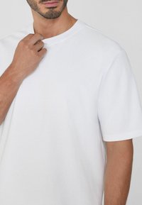 Bílý krátký rukáv tričko s kulatým výstřihem, vyrobené z hladké bavlněné tkaniny, s volným střihem a minimalistickým designem bez vzorů nebo akcentů.