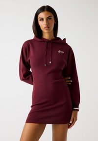 Abito felpa bordeaux con una forma aderente, maniche lunghe e tasca frontale. Finiture in hardware argentato e logo del brand ricamato sul petto.
