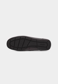 Semelle de chaussure noire avec motif de bande de roulement texturé et logo "ALDO" sur fond gris clair, vue par le dessous.