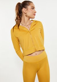 Completo sportivo giallo in due pezzi composto da una felpa corta con zip e leggins a vita alta, realizzato in un materiale morbido e elasticizzato.