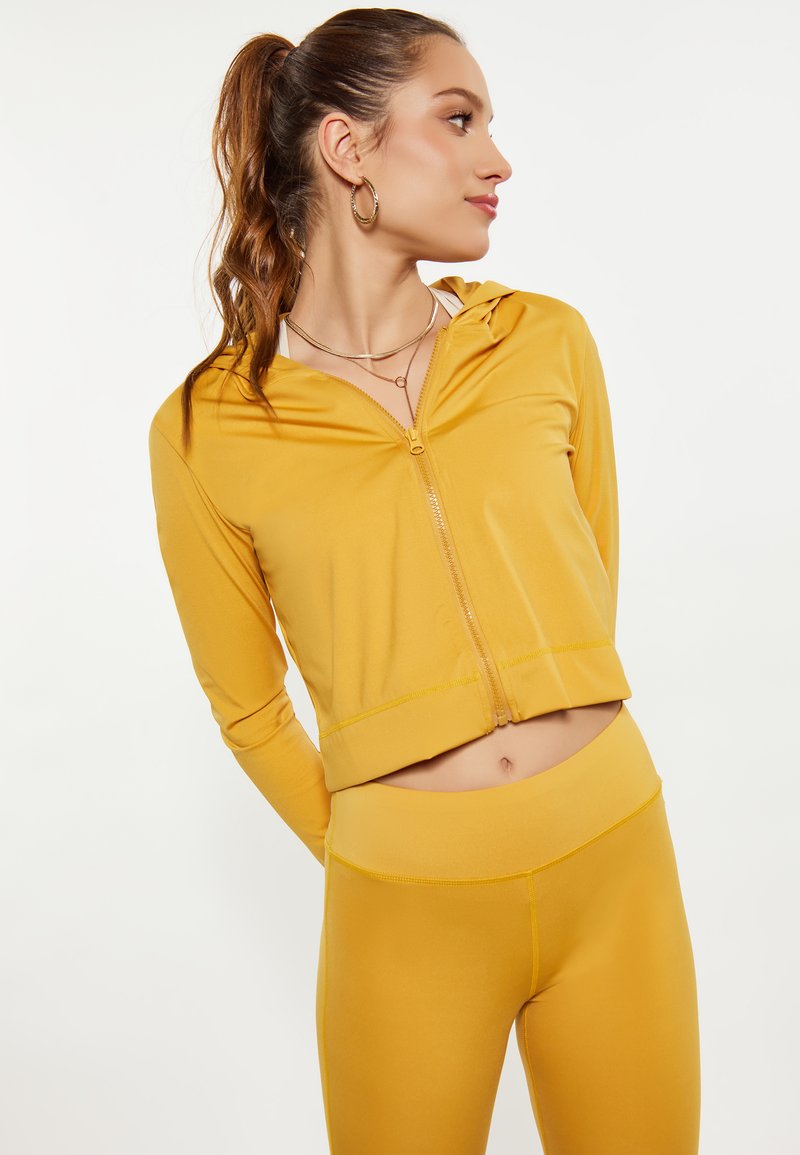 Completo sportivo giallo in due pezzi composto da una felpa corta con zip e leggins a vita alta, realizzato in un materiale morbido e elasticizzato.