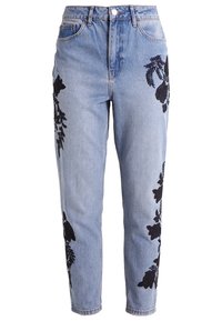 Světlé modré džíny s vysokým pasem, zdobené černou květinovou výšivkou na vnějších stranách a volným střihem.