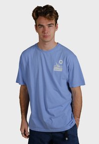 Ljusblå bomullströja med rund hals, korta ärmar och ett framsidetryck med texten "Trendsplant" och en elefantdesign.