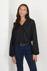 Black blouse with a V-neck and long, puffed sleeves; features a dotted texture. Paired with dark blue jeans and a black belt with a gold buckle.
