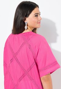 Tunic rosa brillante con maniche corte, caratterizzata da dettagli in pizzo disposti a incrocio. Tessuto morbido con scollatura rotonda e vestibilità comoda.