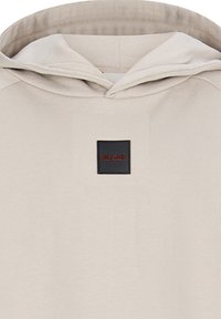 Felpa beige con cappuccio, caratterizzata da un'etichetta quadrata nera con la scritta "RETOUR" in rosso. Texture morbida con design semplice.