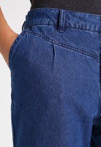 Tmavomodré džíny s vysokým pasem, obsahující kapsu, jemnou strukturu a jemné detaily v odstínu.