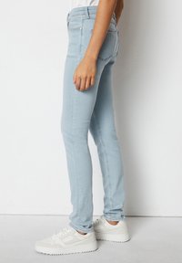 Jeans skinny de un azul claro, fabricados en denim, con una cintura de altura media, diseño de cinco bolsillos y una silueta ajustada, combinados con zapatillas blancas.