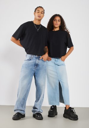 T-shirts noirs surdimensionnés associés à un jean bleu clair et à une jupe bleu clair. Baskets noires épaisses avec une finition texturée.