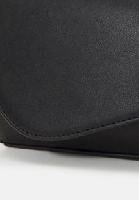 Czarna skórzana kopertówka o gładkiej fakturze, z zaokrągloną klapką i kontrastowym przeszyciem. Kompaktowy design odpowiedni na niezbędne drobiazgi.