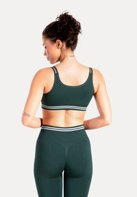 Ciemnozielony sportowy biustonosz z podwójnym paskiem i białymi akcentami, zestawiony z dopasowanymi wysokim stanem legginsami dla spójnego wyglądu.