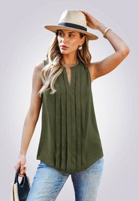 Top sin mangas color verde oliva con pliegues verticales, escote redondo y un ligero corte en forma de V; combinado con jeans de color azul claro y un bolso de mimbre.