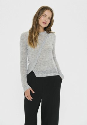 Hellgrauer Strickpullover mit diagonaler Knopfverschluss, langen Ärmeln und einem leicht asymmetrischen Saum, kombiniert mit schwarzen Hosen.