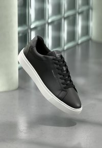 Sneaker din piele neagră cu un finisaj neted, talpă din cauciuc alb și sireturi negre, având logo-ul "GANT" pe lateral.