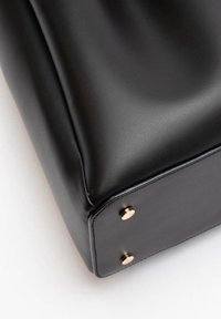 Zwarte leren tas met een gladde textuur, hoekige vorm en goudkleurige hardwareaccenten op de onderste hoeken.