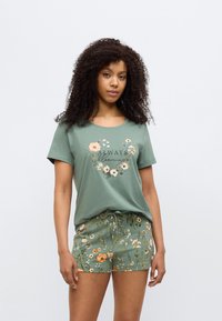 Πράσινο βαμβακερό μπλουζάκι με λουλουδένιο σχέδιο και κείμενο που λέει «Πάντα Ανθίζω». Συνδυασμένο με αντίστοιχα πράσινα σορτς με πολύχρωμο λουλουδένιο μοτίβο.