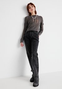 Grijze geribbelde gebreide trui met een lichte transparantie, gecombineerd met zwarte high-waisted jeans en grijze enkellaarsjes met een gespsluiting.
