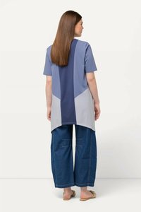 Kortærmet top i blå og grå med et farveblokdesign, med en længere ryg og brede denimbukser med synlige sting.