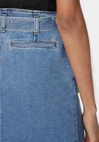 Džínová sukně střední modré barvy s přiléhavým pasem, bočním švem a jednou zadní kapsou. Obsahuje oranžové švy a hladkou texturu.