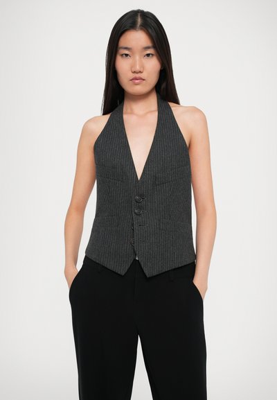 Gilet halter gris foncé avec des rayures verticales, décolleté en V profond, fermeture à cinq boutons et poches accentuées, associé à un pantalon noir.