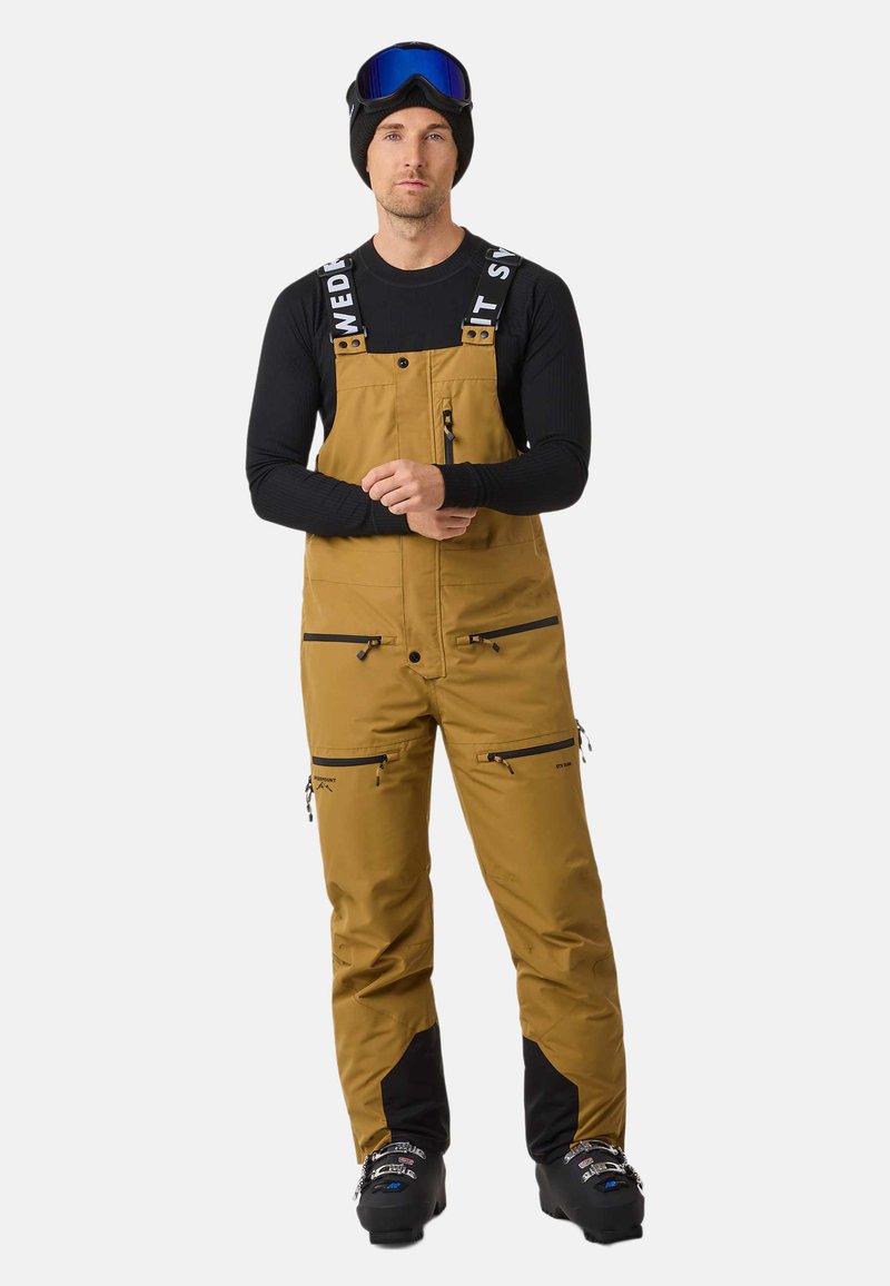 Bruna snöoveraller med svarta detaljer, justerbara remmar, flera fickor med dragkedja och ett slitstarkt tyg som är lämpligt för vinterförhållanden.