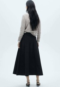 Sort, ankellang nederdel med plissé-detaljer, parret med en lysegrå sweater. Materialet ser blødt ud, og stilen er enkel og svævende.